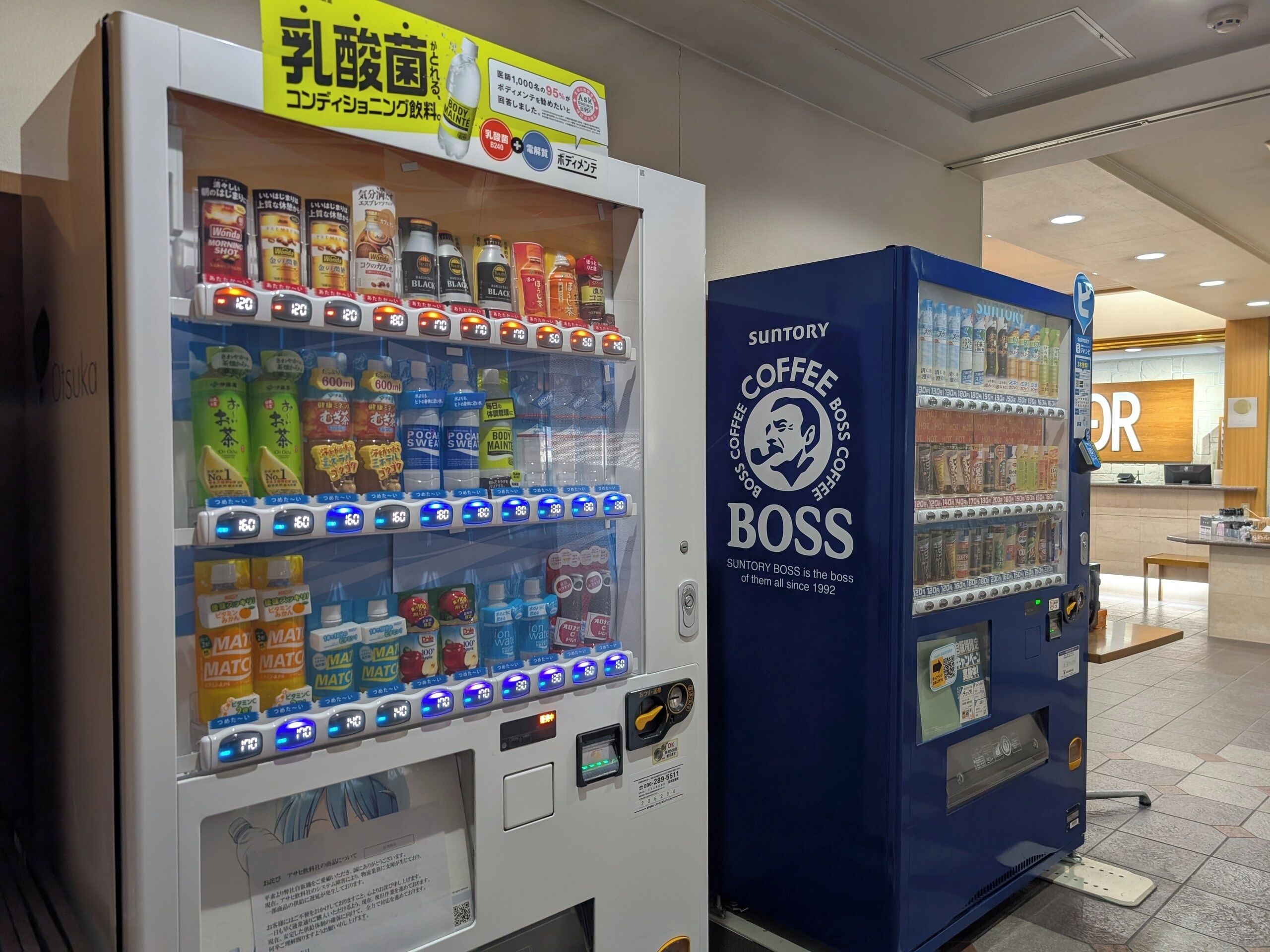 Ein Automat mit verschiedenen Getränken und Snacks, sowie ein Kaffeeautomat mit der Aufschrift 'Suntory Coffee Boss'.