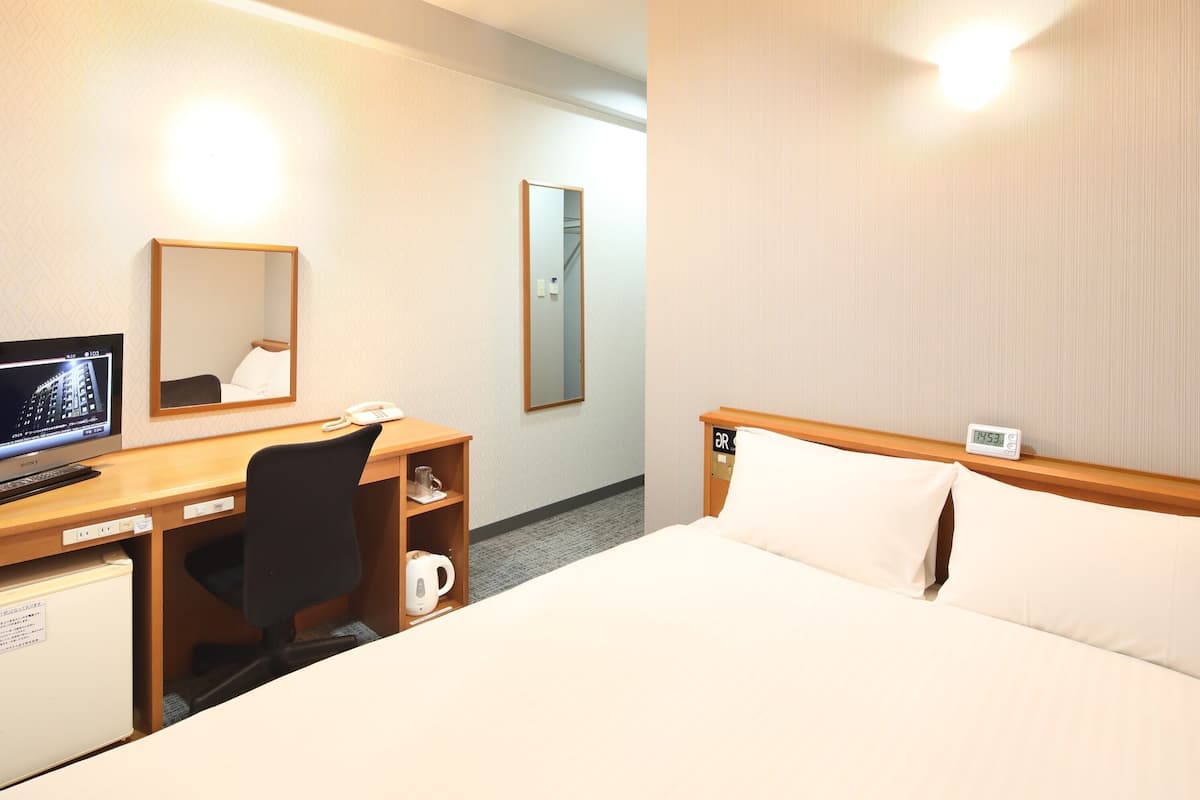 A hotel room with a bed, a desk with a computer monitor, a telephone, and a mirror.