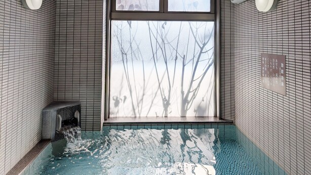 A small indoor pool with a view of bare trees through a window, tiled walls, and a bench. - Green Rich Hotel Aso Kumamoto Airport Artificial Hot Spring Futamata Yunohana (Kikuyo)
