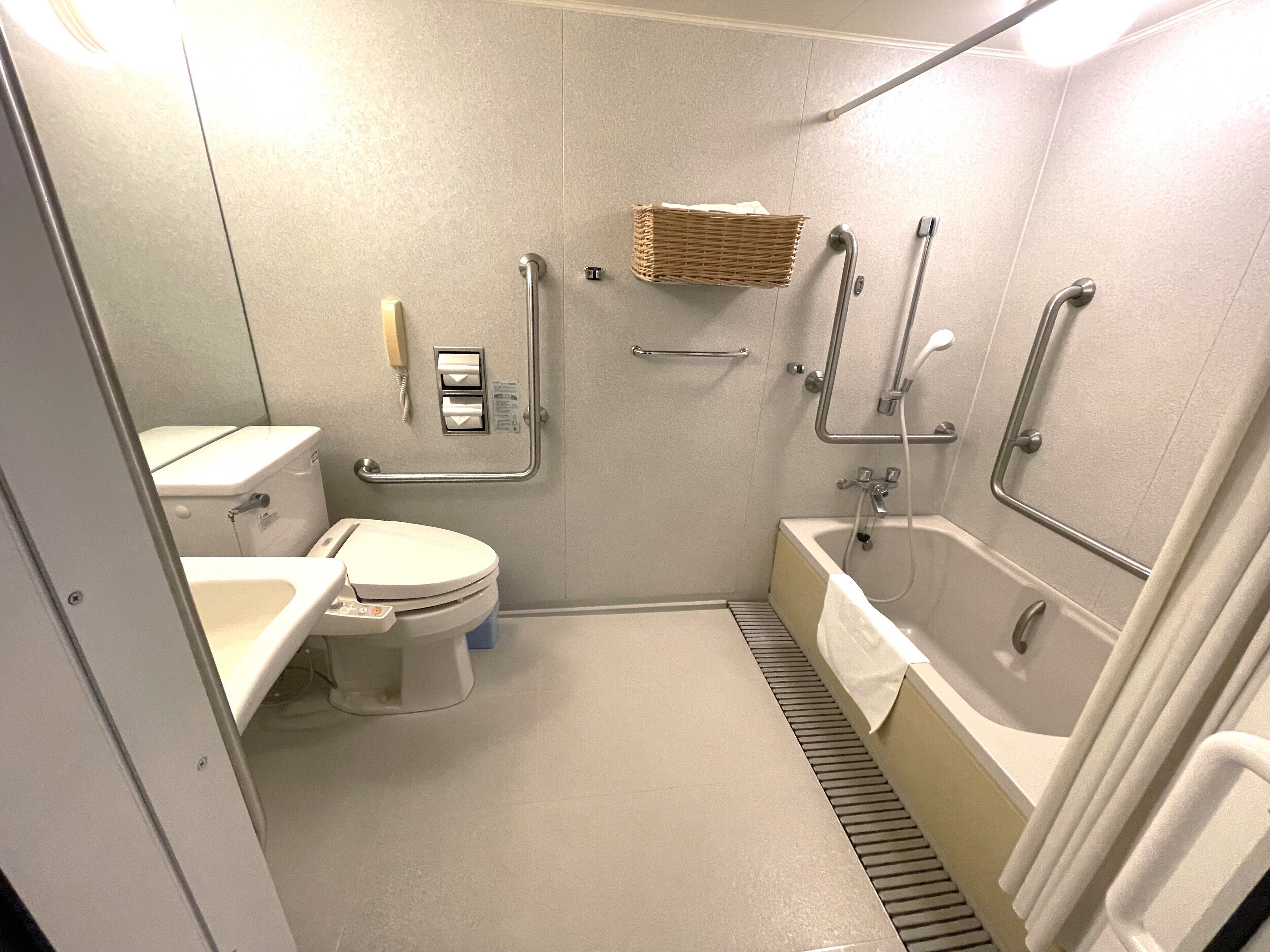 A small, modern bathroom with a toilet, sink, and bathtub. It includes grab bars and a hand dryer.