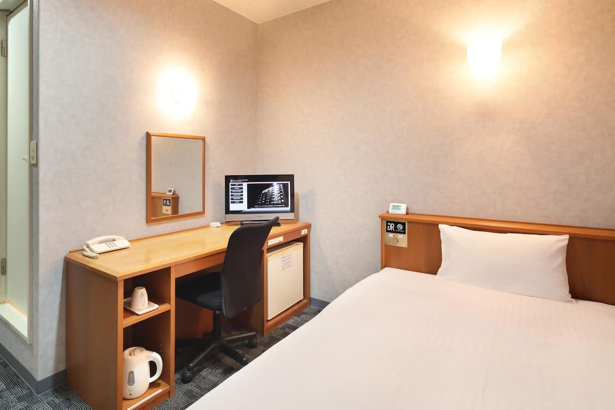 A hotel room with a bed, a desk with a computer, a telephone, a mirror, and a small cabinet.