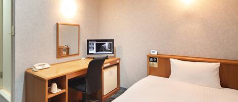 Habitación de hotel con cama, escritorio con computadora, teléfono, espejo y un mueble pequeño.