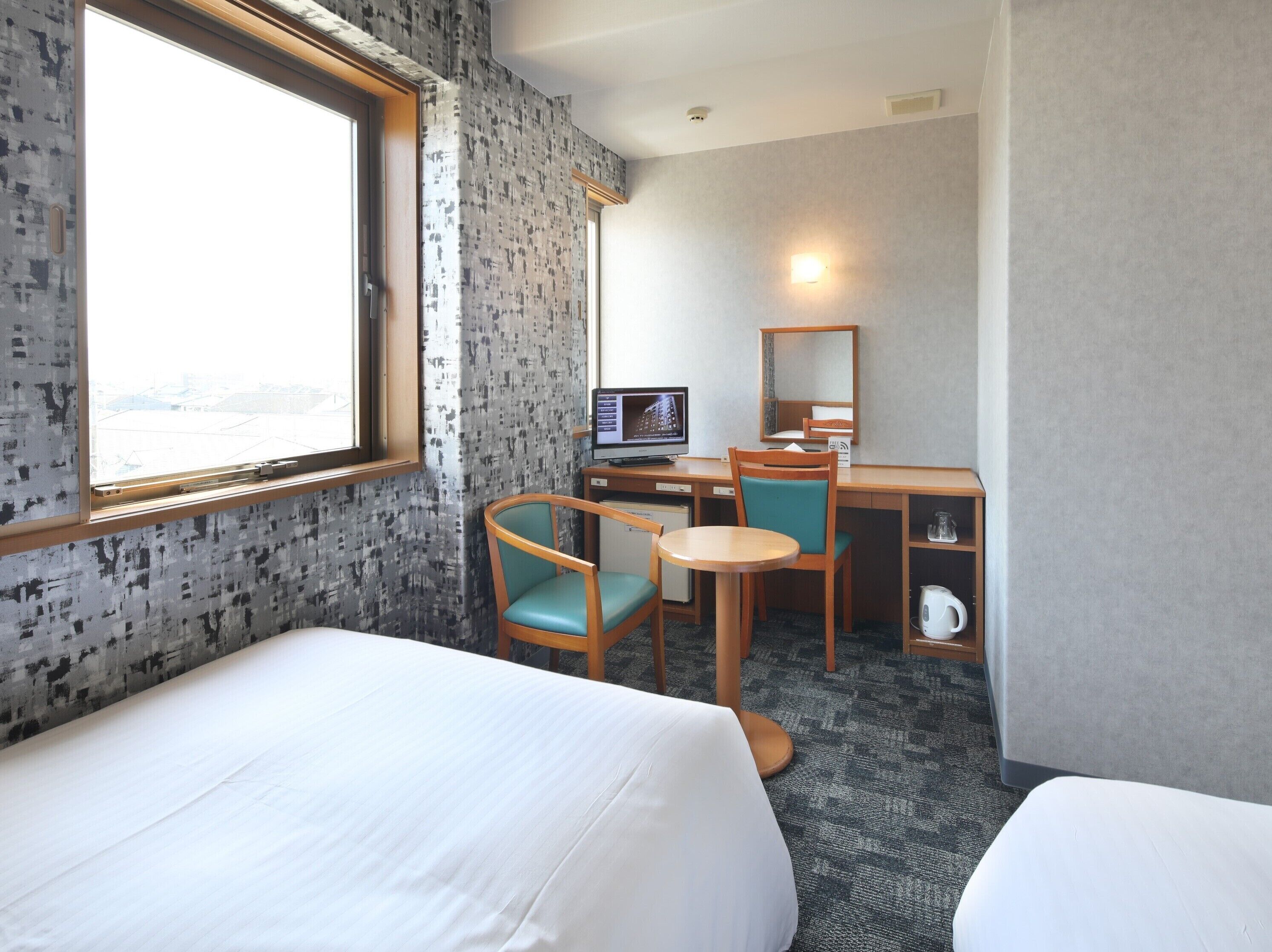 Hotelkamer met twee bedden, een bureau met een computer, een stoel, een kleine tafel en een raam met uitzicht.