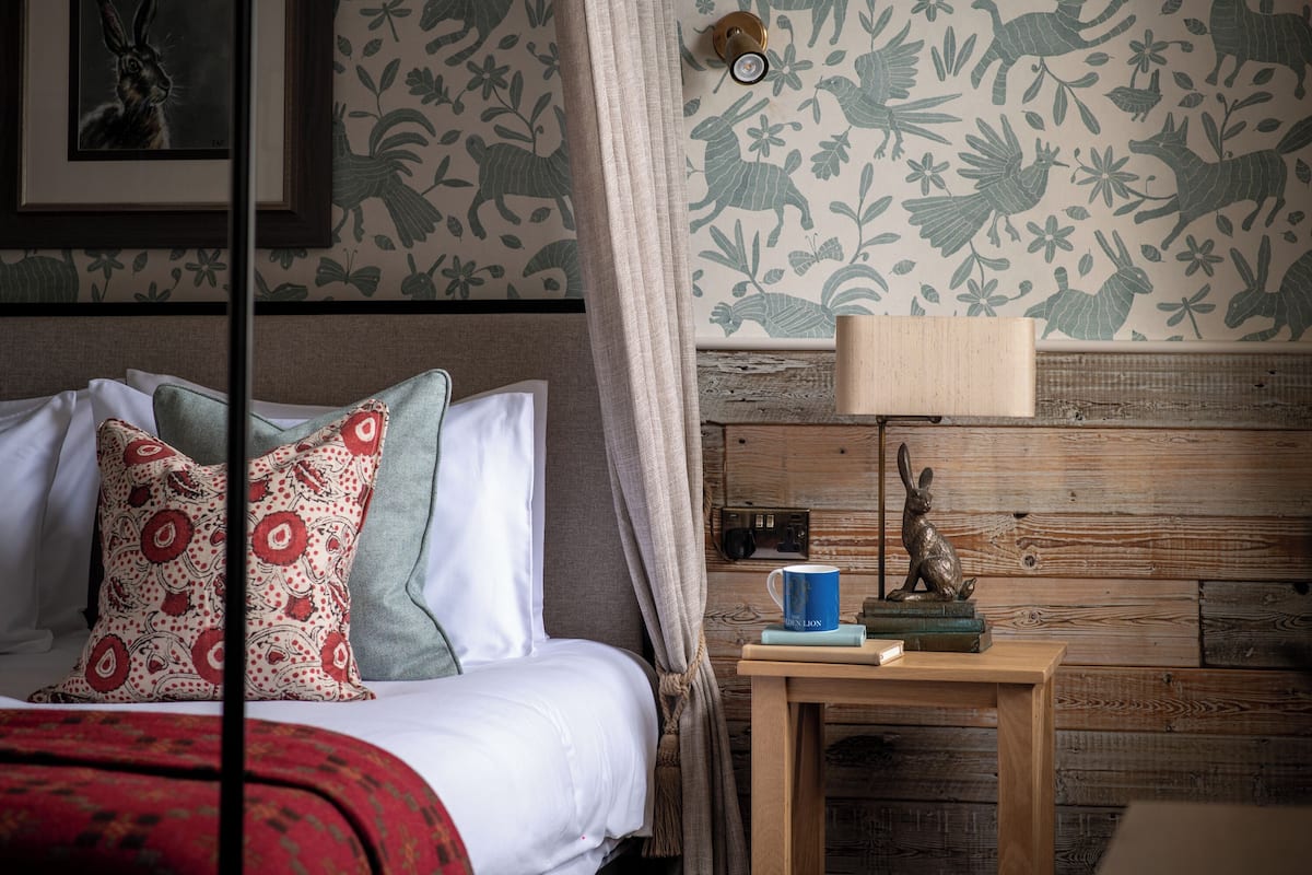 A neatly made bed with patterned pillows, a bedside table with a lamp, and a wall with floral wallpaper.