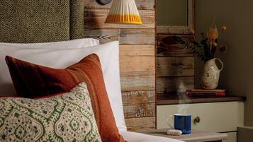 A neatly made bed with patterned pillows, a wooden headboard, a bedside table with a lamp, a vase with flowers, and a book.