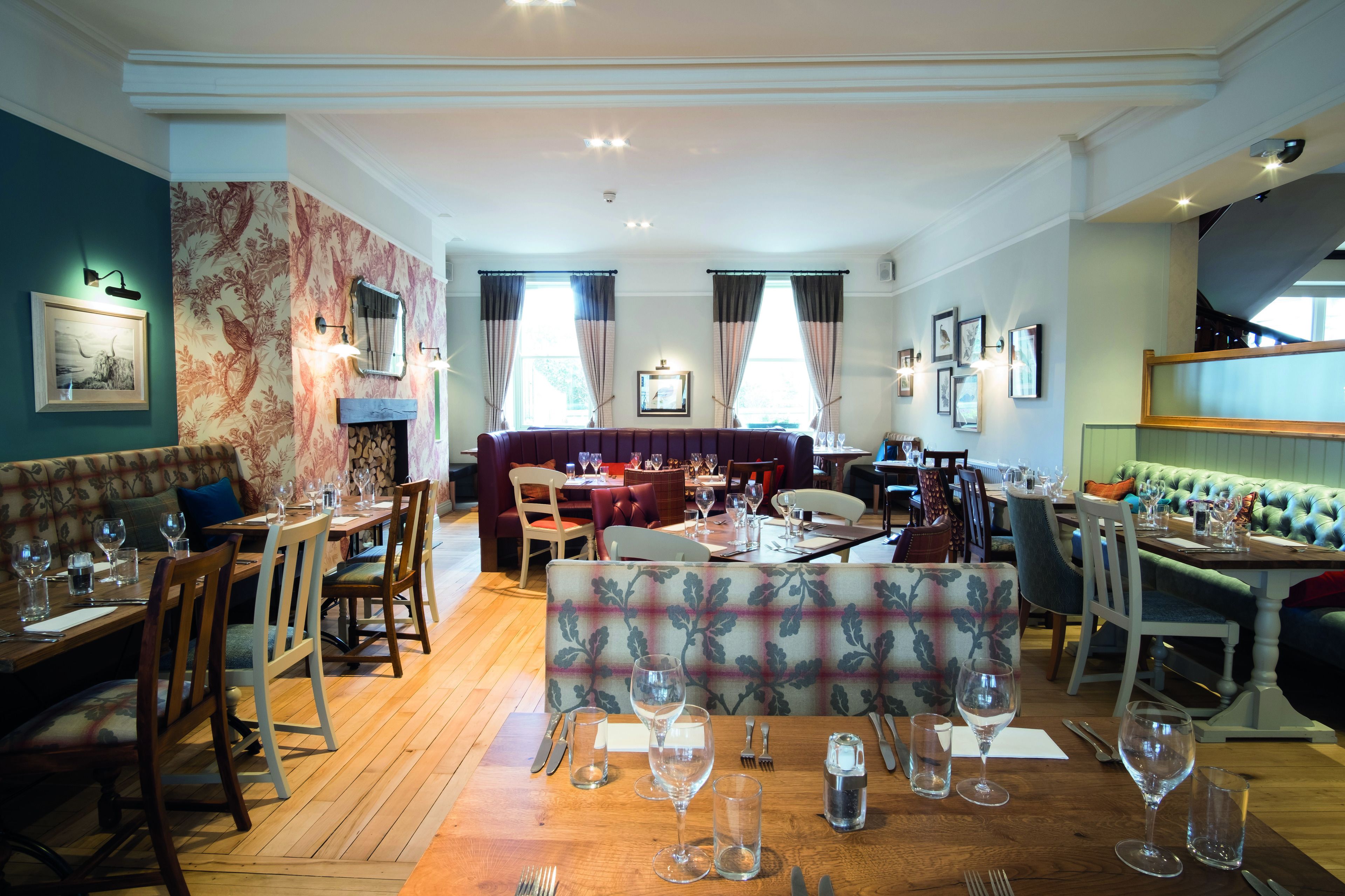 A restaurant with wooden tables and chairs, a patterned sofa, and framed pictures on the walls.