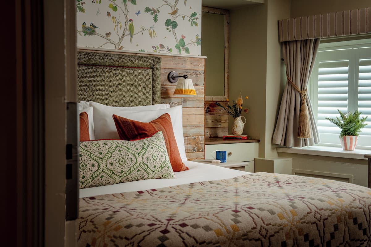 A neatly made bed with patterned bedding, a wall-mounted lamp, and a window with curtains.