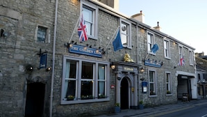 A stone building with a pub sign, flags, and a lion statue. - The Golden Lion (Settle)
