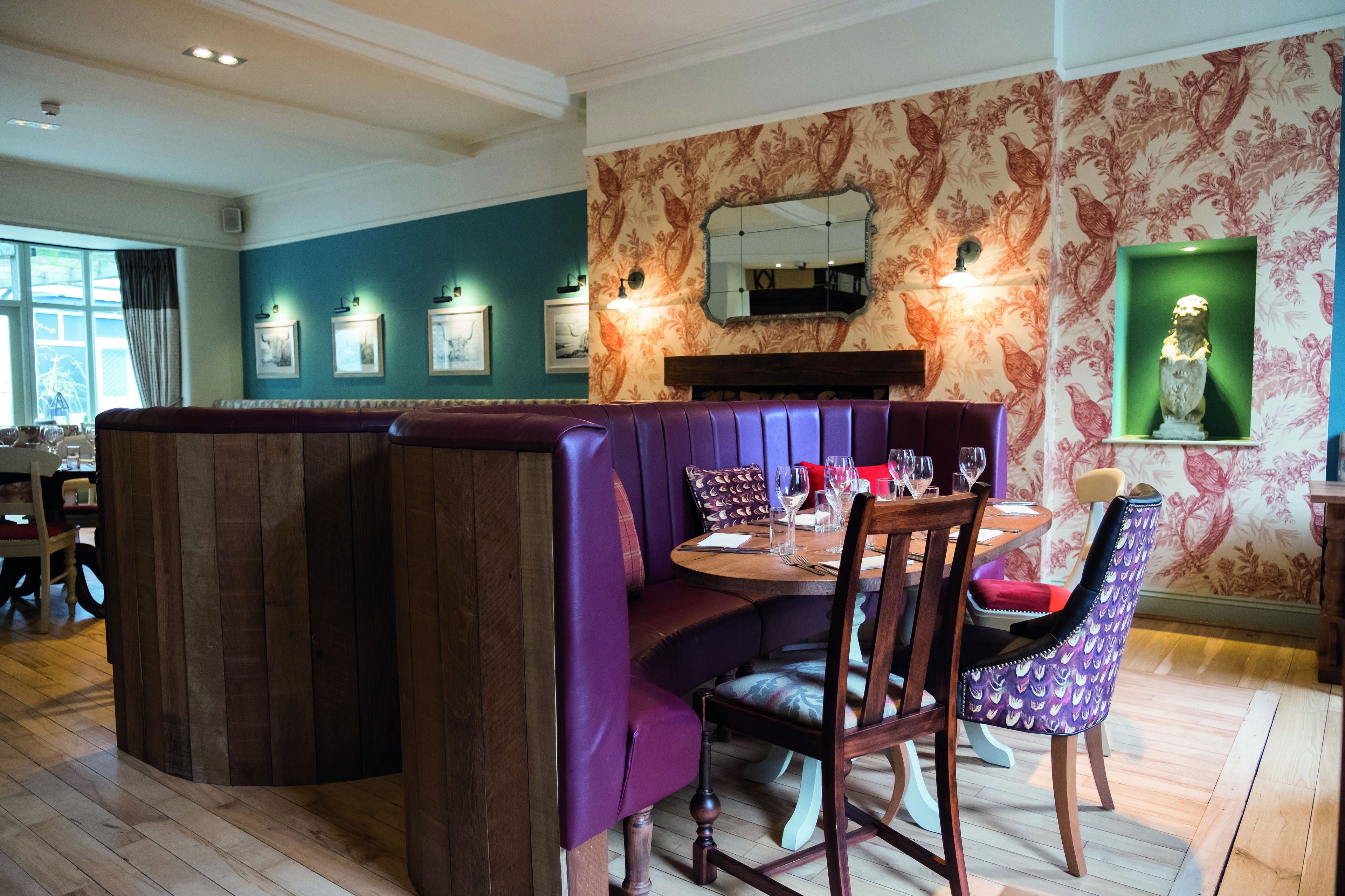 A dining area with a wooden table, purple booth seating, and a patterned wall.