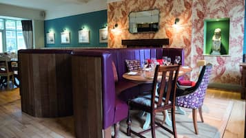 A dining area with a wooden table, purple booth seating, and a patterned wall.