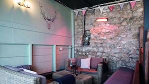 A cozy room with wicker furniture, a stone wall, and a mounted deer head. - The Golden Lion (Settle)
