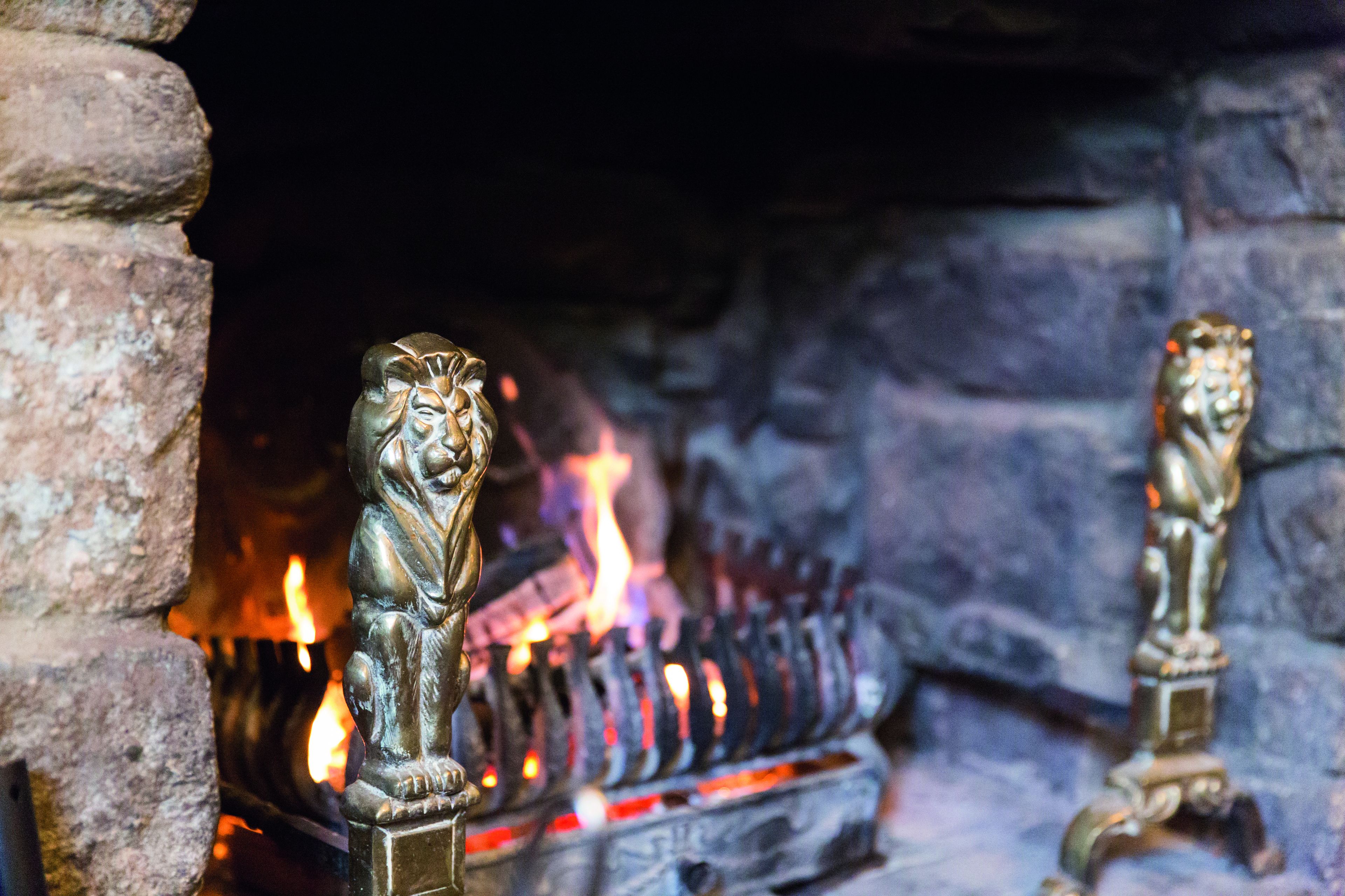 A fireplace with two lion statues and burning logs.