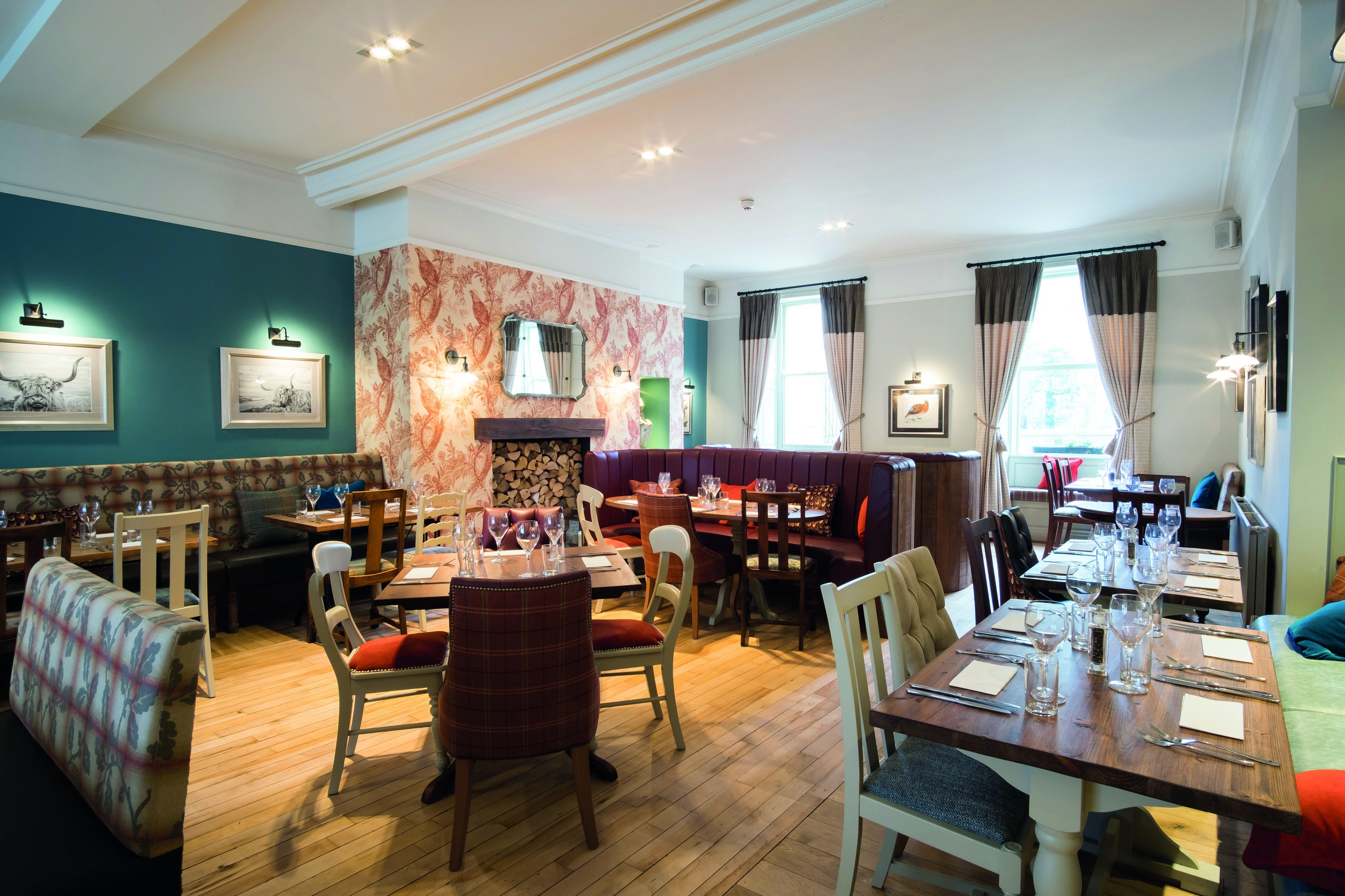 A restaurant with wooden flooring, multiple dining tables and chairs, and a fireplace.