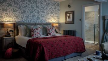 Een slaapkamer met een bed, nachtkastjes, een bloemenbehang muur, een lijst met een afbeelding en een glazen deur naar een badkamer.