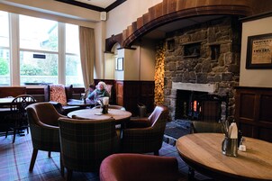 Un pub acogedor con chimenea de piedra, sillas a cuadros y un letrero que dice 'No hay habitaciones disponibles'.