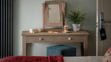 A wooden desk with a mirror, a potted plant, a cup, and a small table with a candle and a brush.