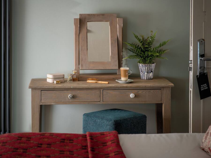 A wooden desk with a mirror, a potted plant, a cup, and a small table with a candle and a brush.