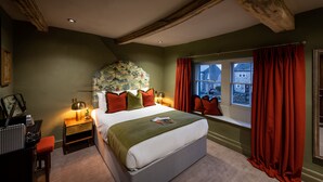 Un dormitorio con una cama grande, una ventana con cortinas rojas, una mesita de noche con lámpara y vistas al exterior.