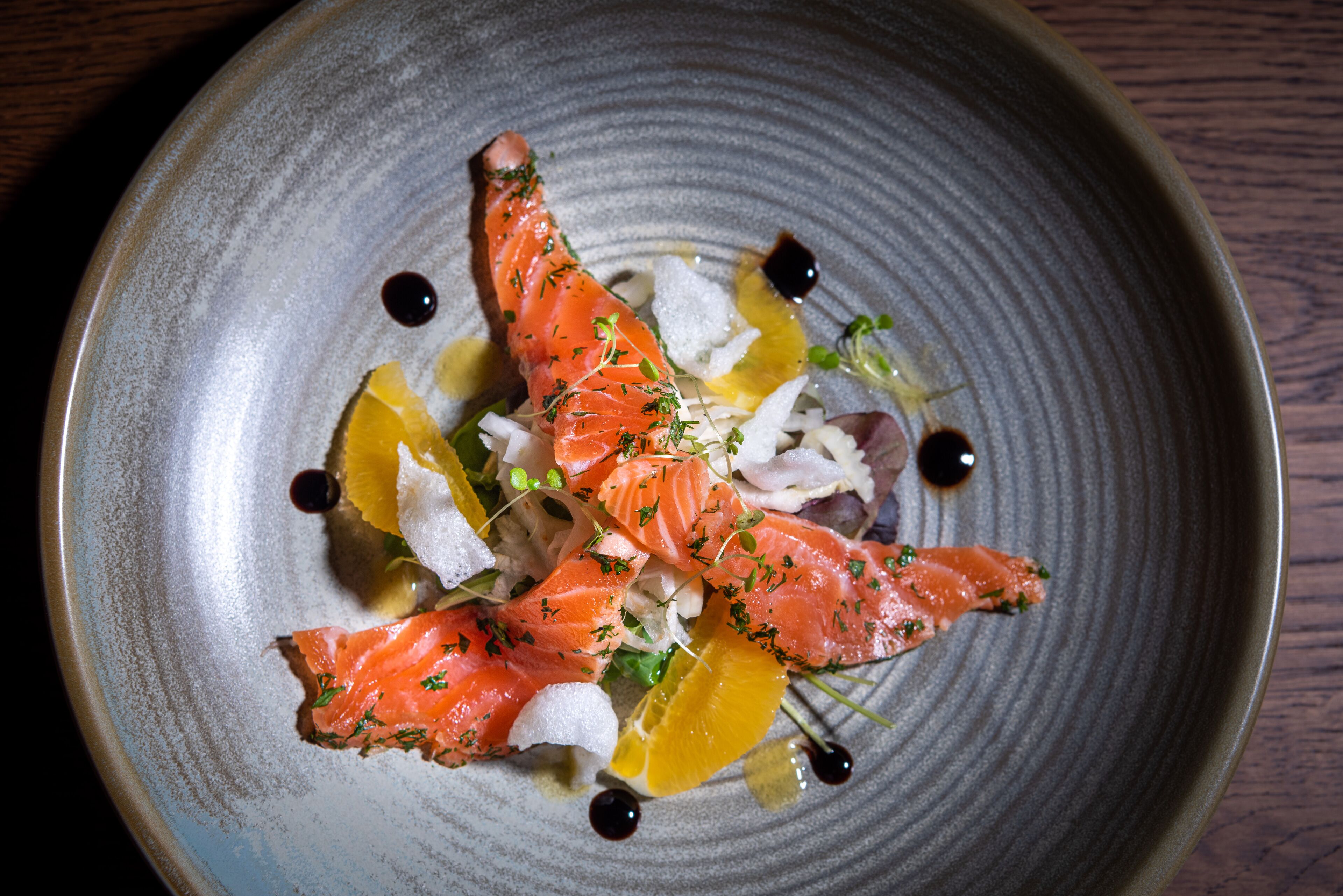 Een bord met zalm, citrusvruchten en garnering.