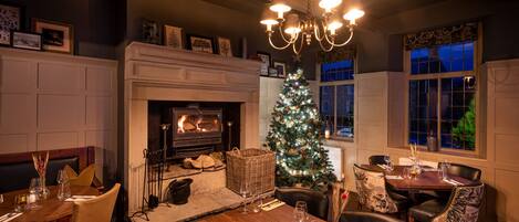 Un rincón comedor acogedor con chimenea, árbol de Navidad y candelabro.