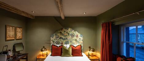 Um quarto com uma cama, duas mesas de cabeceira, uma escrivaninha, uma cadeira e uma janela com cortinas.
