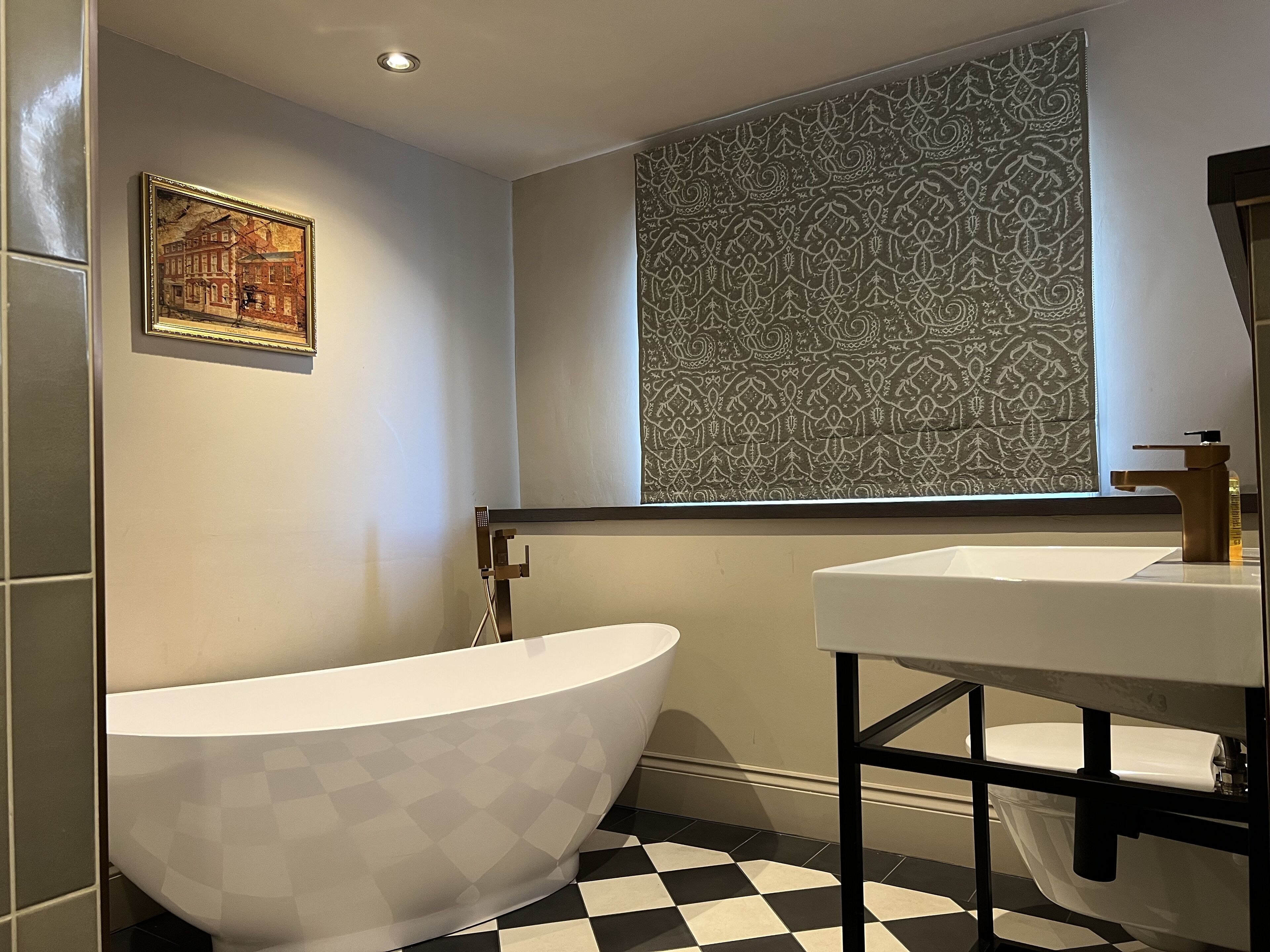 A bathroom with a freestanding bathtub, a sink, and a patterned window.
