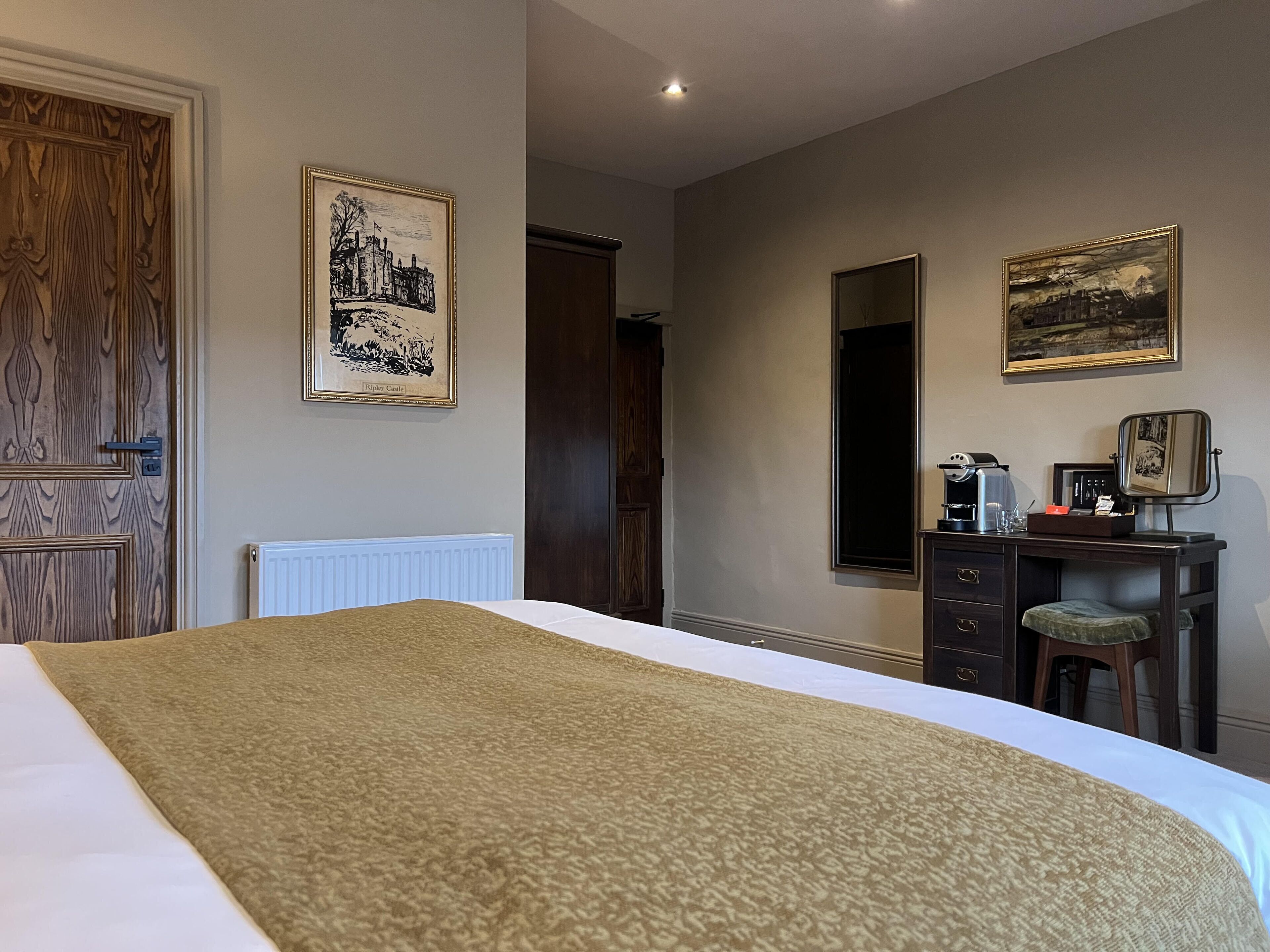 A hotel room with a bed, a dresser, a mirror, and framed artwork on the walls.