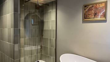 A modern bathroom with a glass-enclosed shower, a white freestanding bathtub, and a framed cityscape painting on the wall.