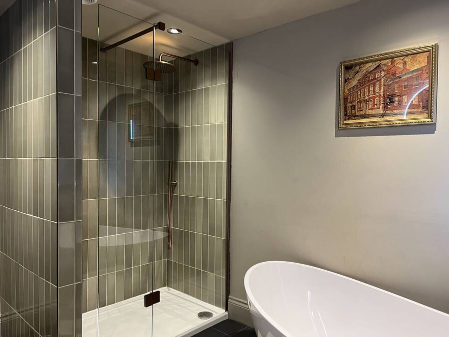 A modern bathroom with a glass-enclosed shower, a white freestanding bathtub, and a framed cityscape painting on the wall.