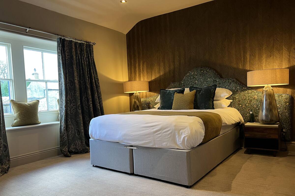 A modern bedroom with a large bed, two bedside tables, a window with curtains, and a patterned headboard.
