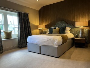 A modern bedroom with a large bed, two bedside tables, a window with curtains, and a patterned headboard.