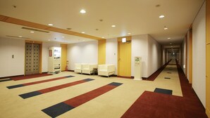 A hotel hallway with a carpeted floor, seating area, and a reception desk. - Highness Hotel Kurume (Kurume)
