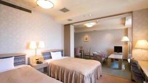 A hotel room with two beds, a desk, a chair, a TV, and a mirror. - Highness Hotel Kurume (Kurume)