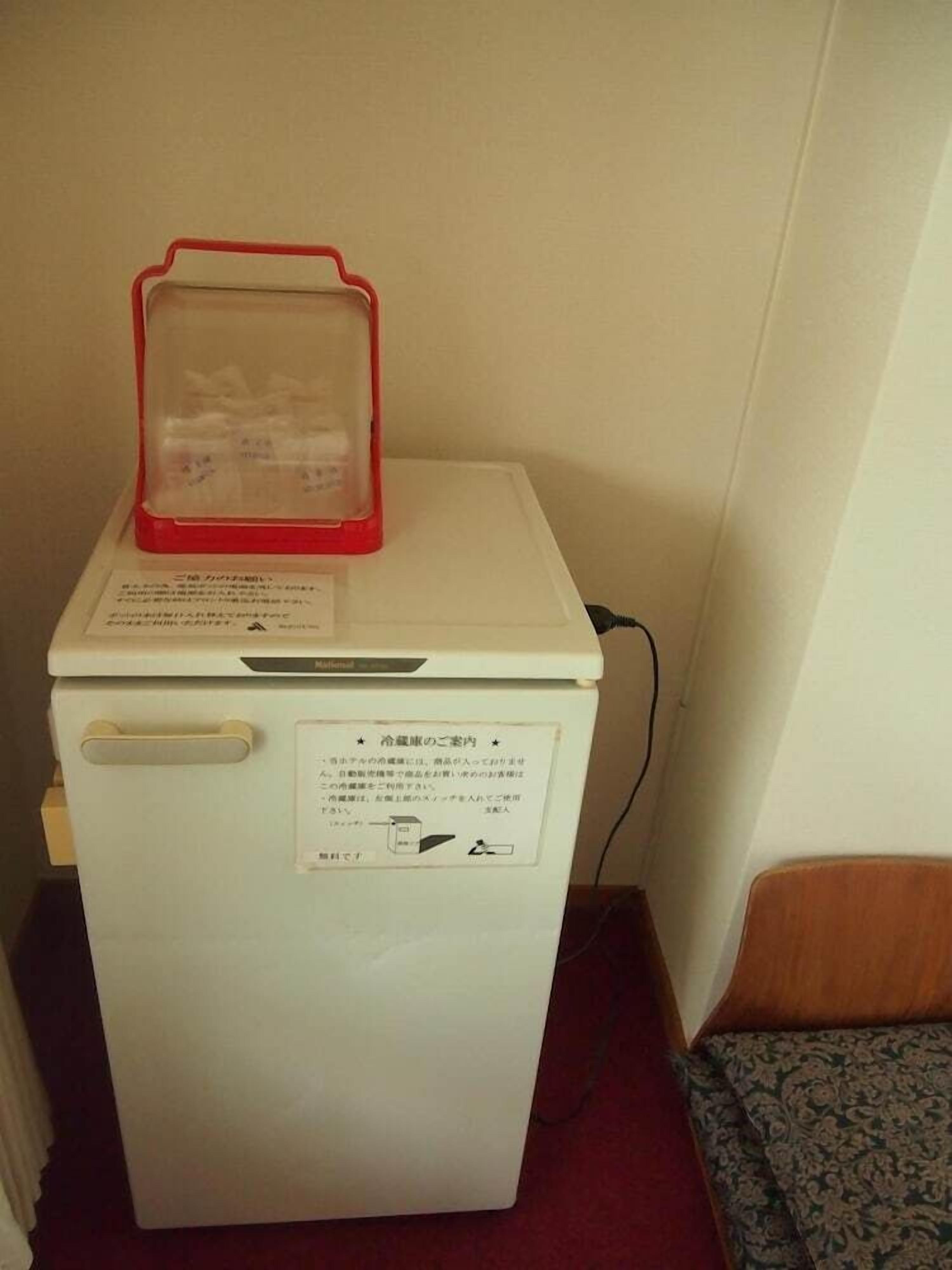 A small white refrigerator with a red plastic container on top, a handle on the side, and a label with text.