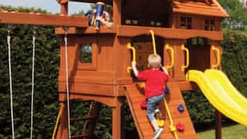 A wooden play structure with a slide, climbing wall, and rope ladder.