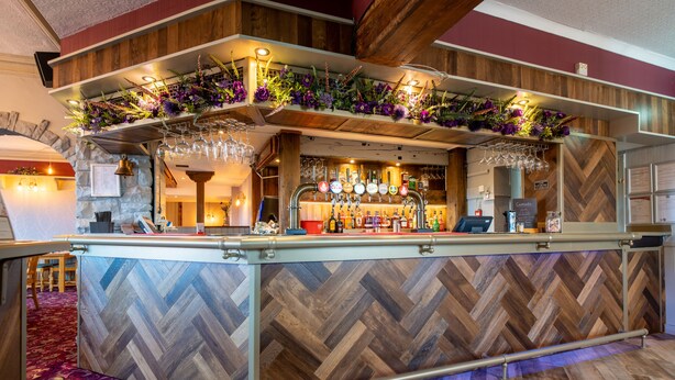 A bar area with a wooden herringbone floor, a counter with a metal railing, and a variety of bottles and glasses. - The Sitwell Arms Hotel (Sheffield)