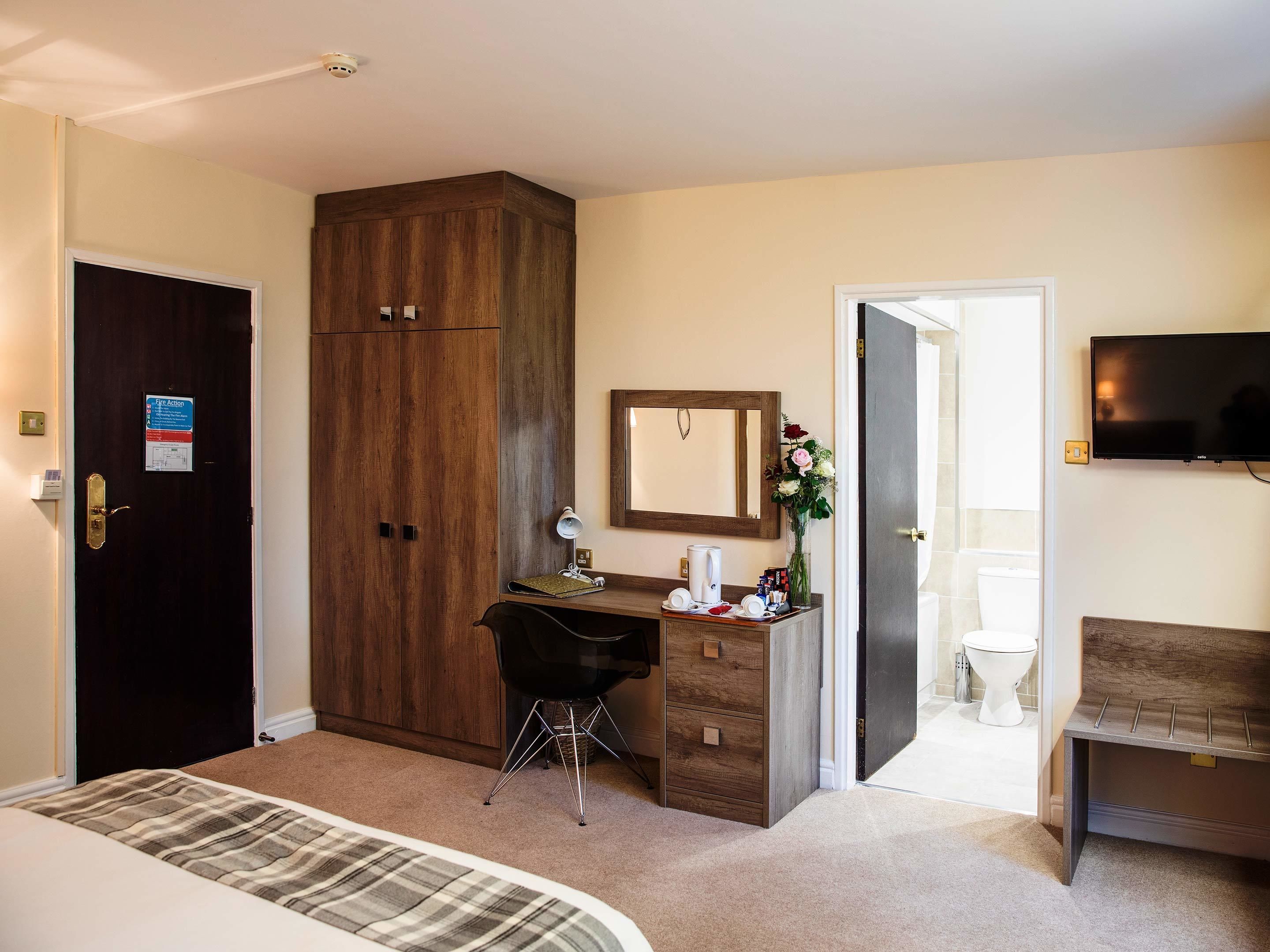 Ett hotellrum med en säng, ett skrivbord med en stol, en garderob, en spegel, en tv och ett badrum med toalett och handfat.