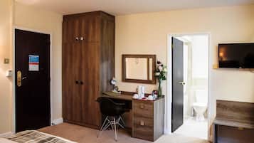A hotel room with a bed, a desk with a chair, a wardrobe, a mirror, a television, and a bathroom with a toilet and sink.