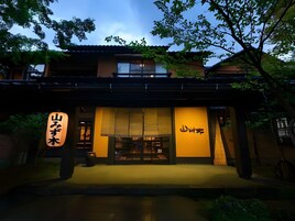 Edificio japonés tradicional con un letrero, un acceso cubierto y un pequeño jardín.