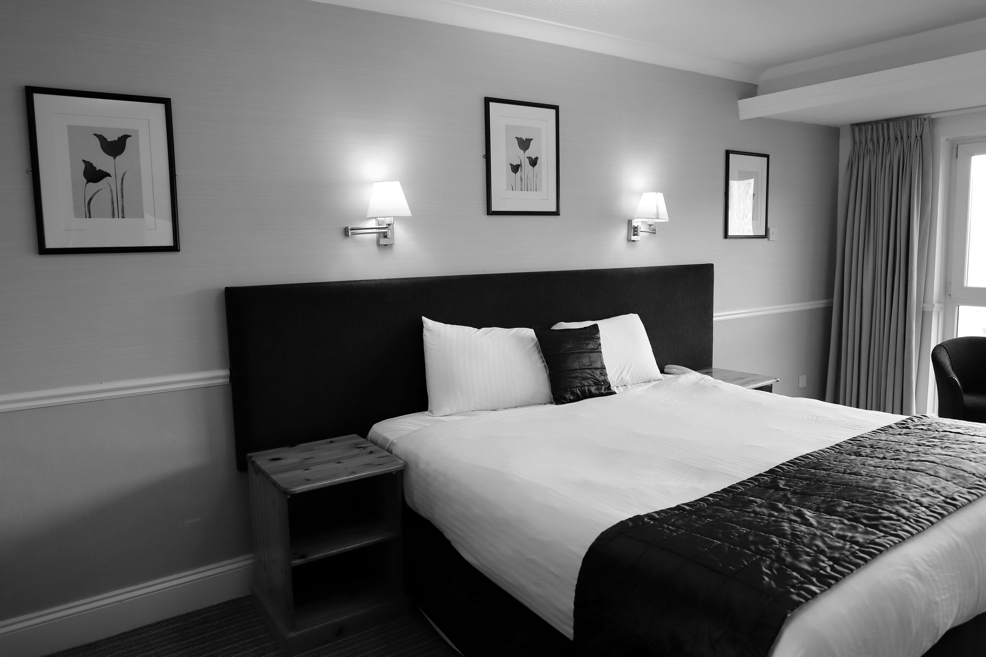 A hotel room with a large bed, two bedside lamps, a nightstand, and two framed pictures on the wall.