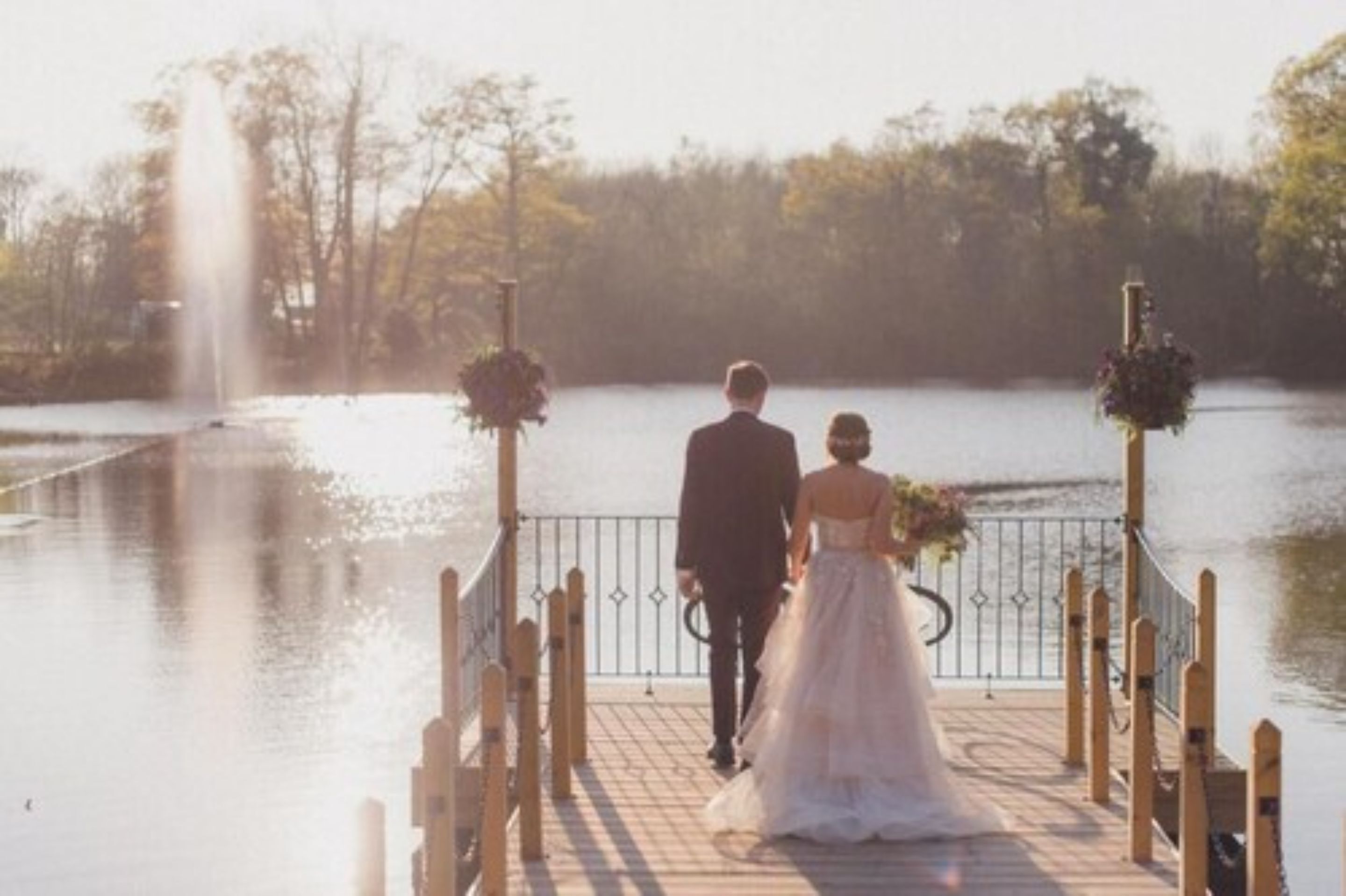 A wooden dock leading to a body of water with a fountain in the background.