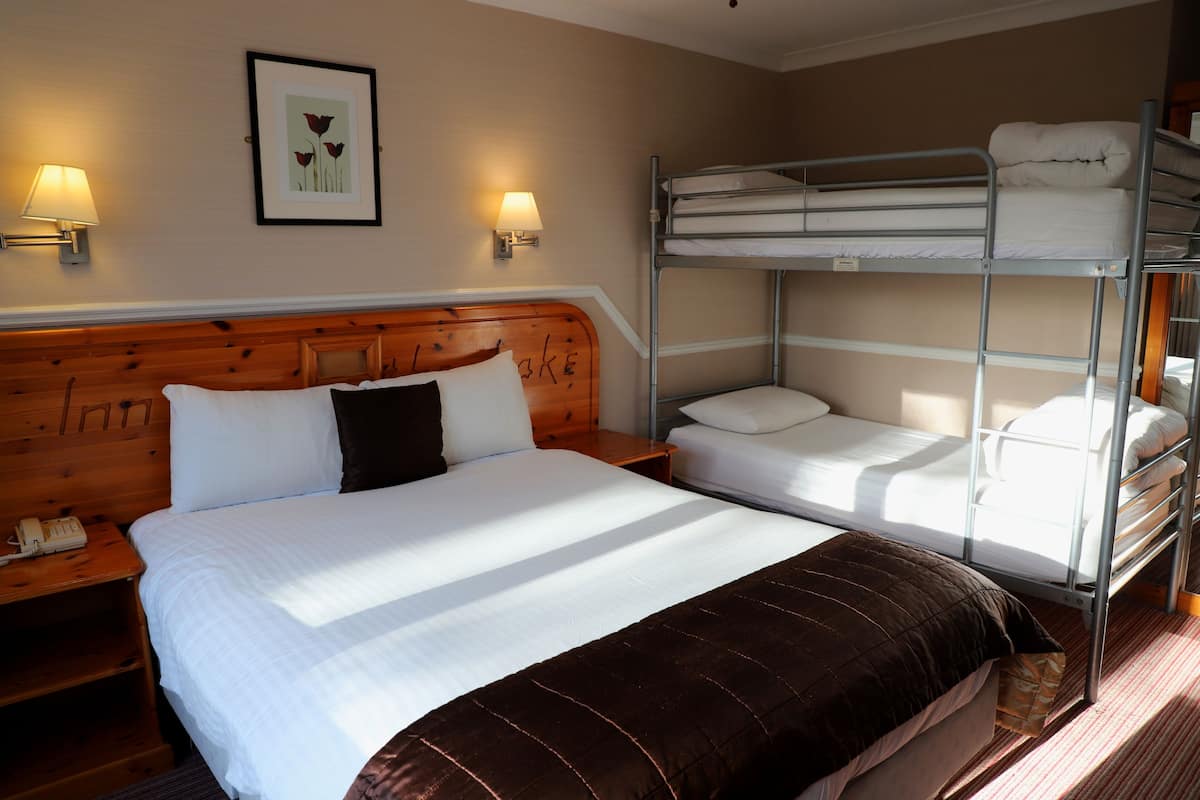 A hotel room with a wooden headboard bed, a lower bunk bed, and a bedside table with a lamp and phone.