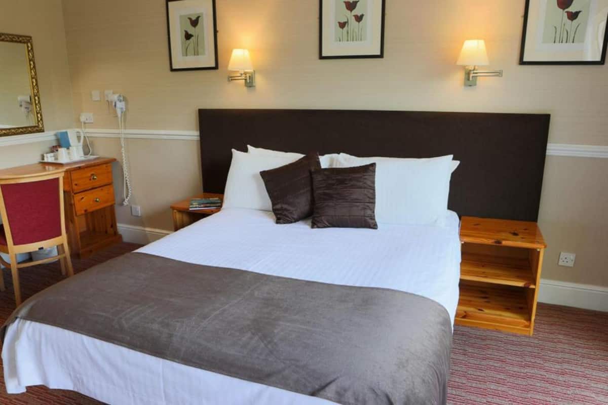 A neatly made bed with a dark headboard, a bedside table with a lamp, and a small wooden nightstand.