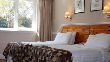 Habitación de hotel con dos camas, un ventanal grande con cortinas, lámparas fijadas a la pared y cuadros con motivos florales.