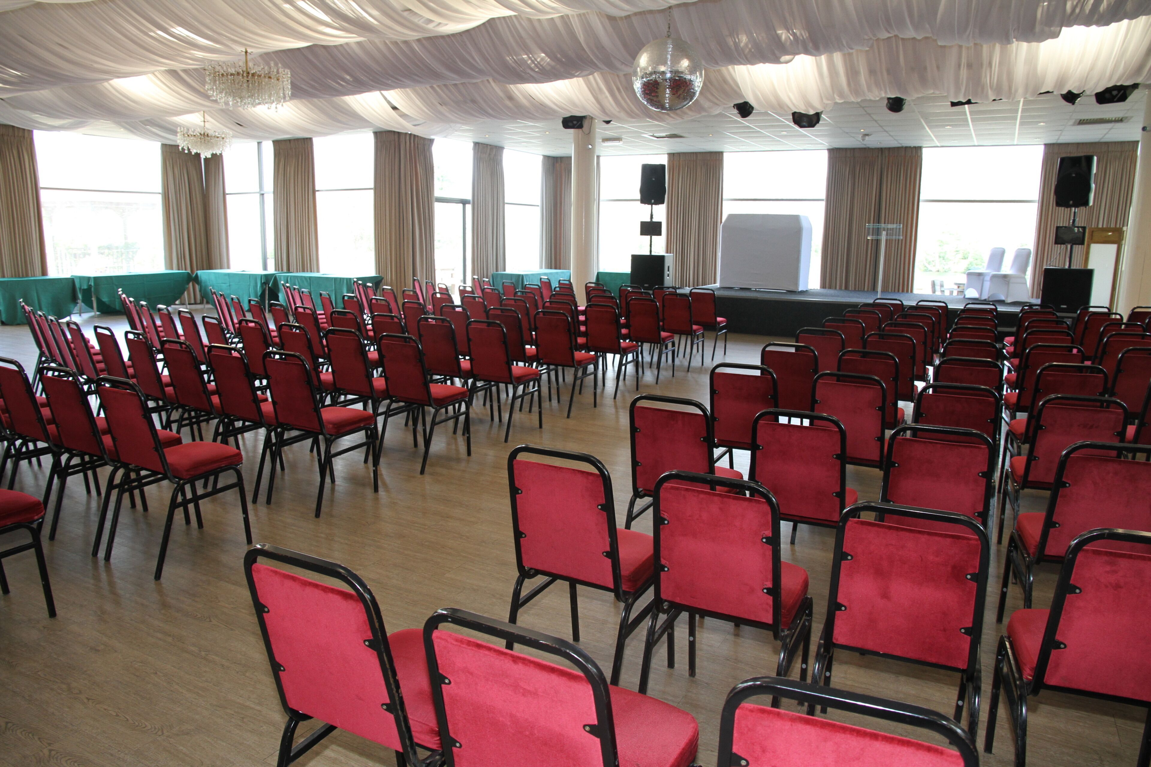 A conference room with rows of red chairs, a stage, and large windows.