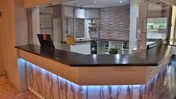 A reception desk with a marble base and a glass top, surrounded by a modern interior with a patterned wall and a plant.