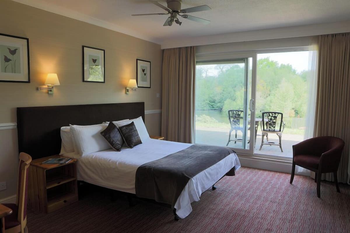 A hotel room with a bed, a chair, a table, a ceiling fan, and a view of the outdoors.