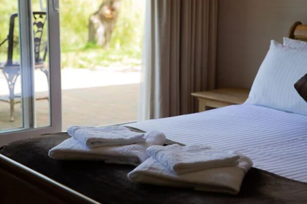 A hotel room with a bed, a window with curtains, and a view of a tree outside. - The Inn on the Lake Hotel (Gravesend)