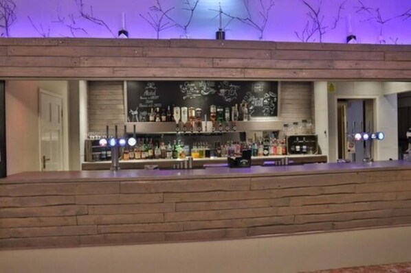 Un espace bar avec un comptoir en bois, des étagères remplies de bouteilles de toutes sortes et un menu écrit à la craie.