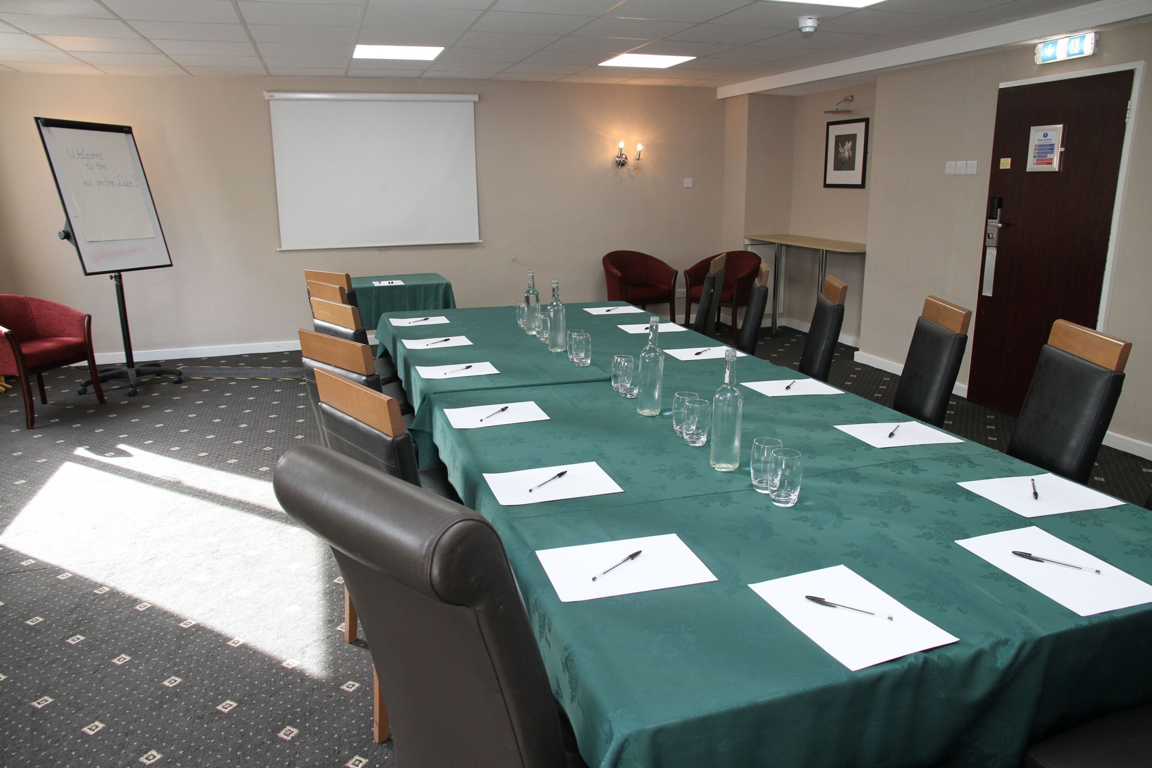 A conference room with a long table, chairs, a whiteboard, and a projector screen.